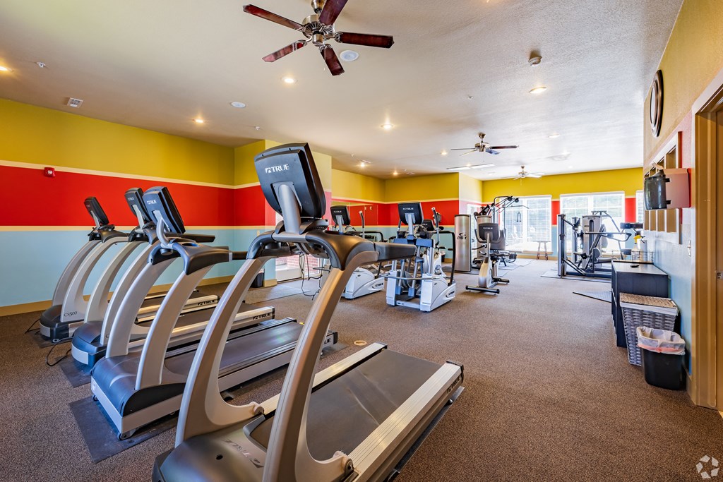 a gym with cardio equipment and a ceiling fan