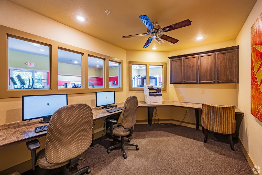 two computer desks and two chairs in a room with a ceiling fan