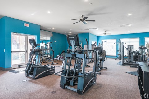 a gym with various cardio machines and a ceiling fan