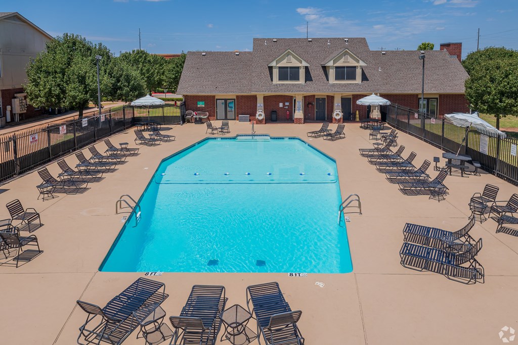an aerial view of a swimming pool with chairs and a building in the background