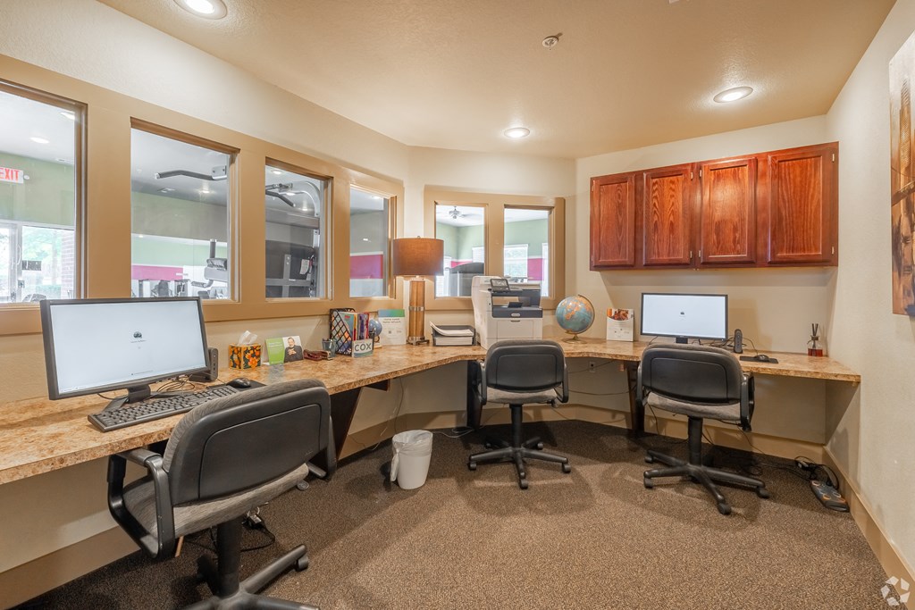 three desks with computers and chairs in an office with windows