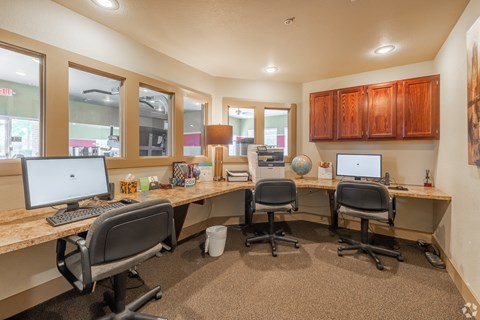 three desks with computers and chairs in an office with windows