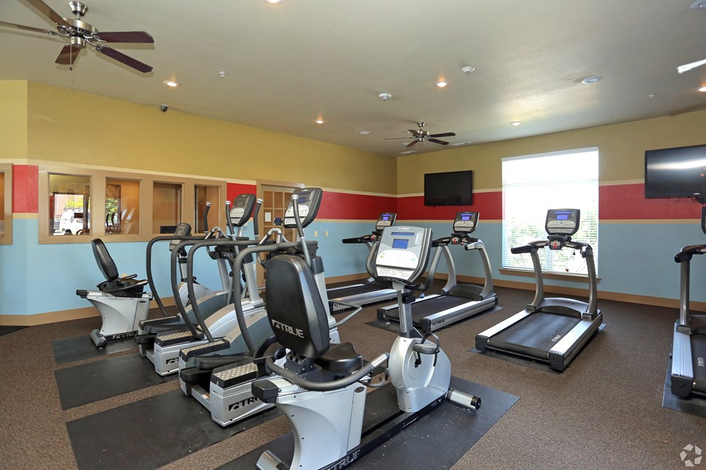 a gym with cardio equipment and a tv