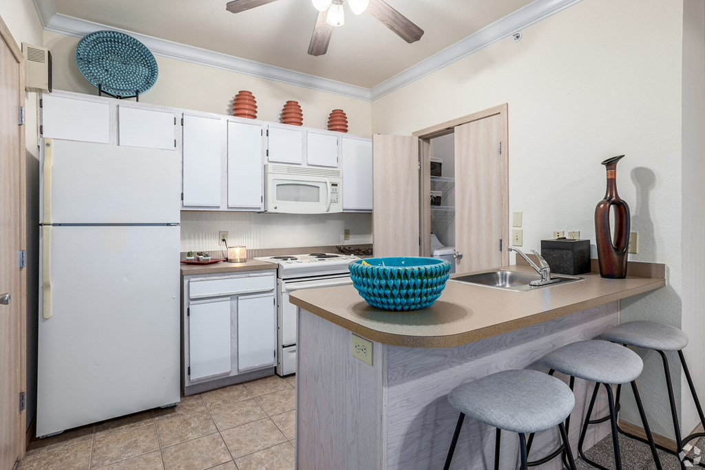 a kitchen with white appliances and a bar with three stools