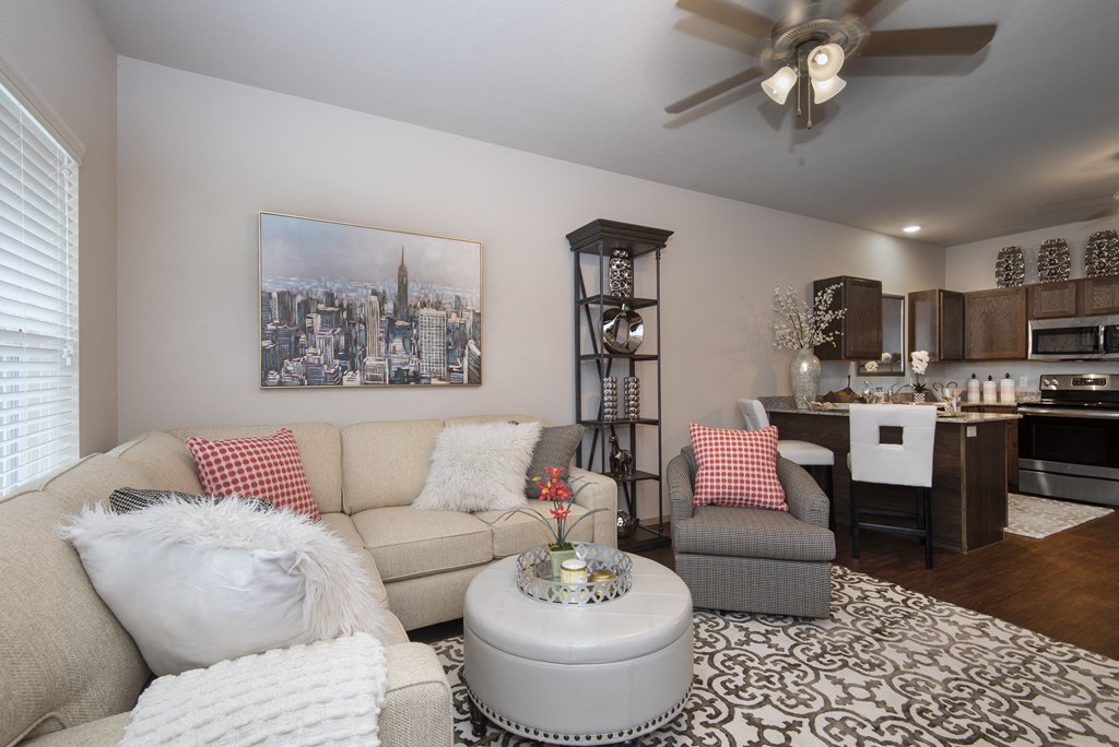 A living room with a beige couch, a grey armchair, a white coffee table, and a painting of a city skyline on the wall.