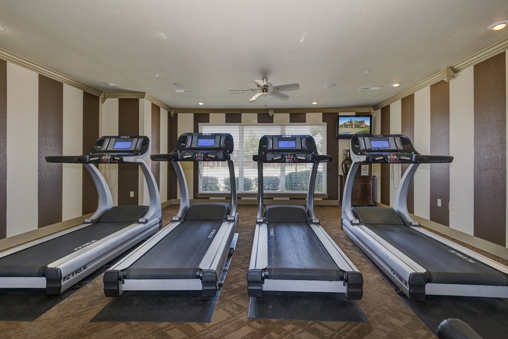 a gym with four treadmills and a ceiling fan
