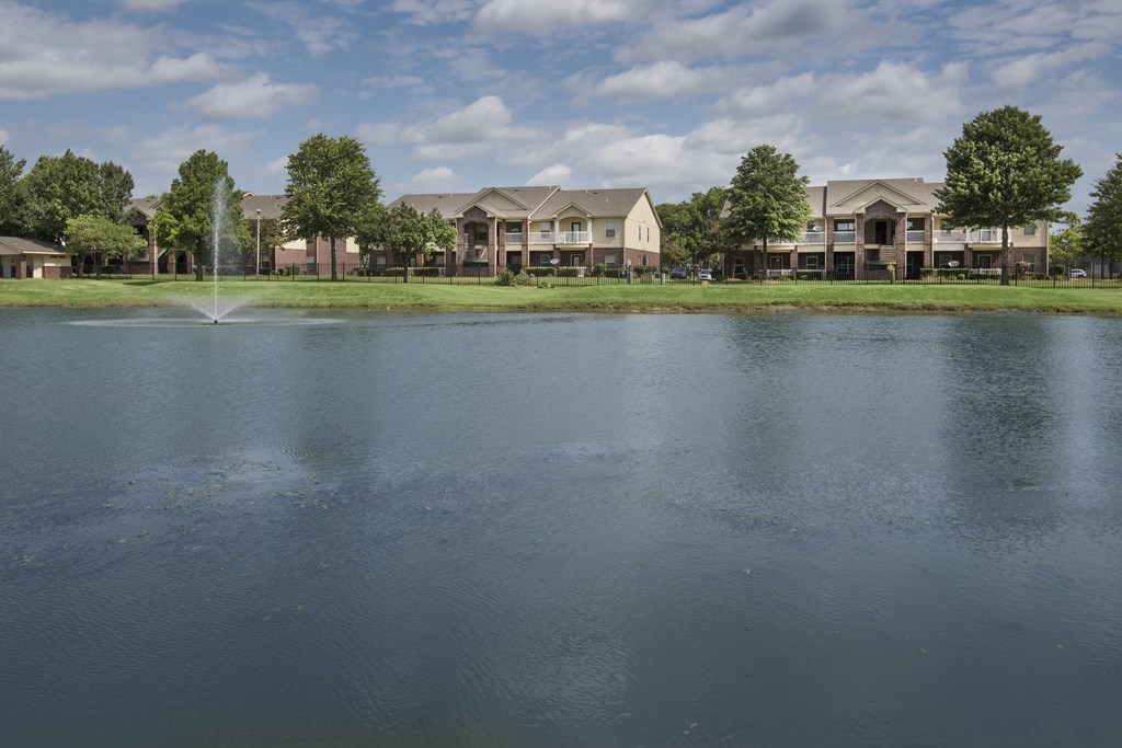A fountain in the middle of a lake in front of apartment buildings.