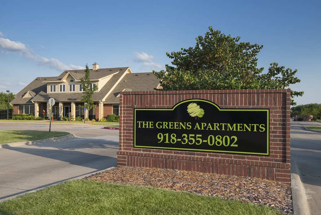 A sign for The Greens Apartments with a phone number on it.