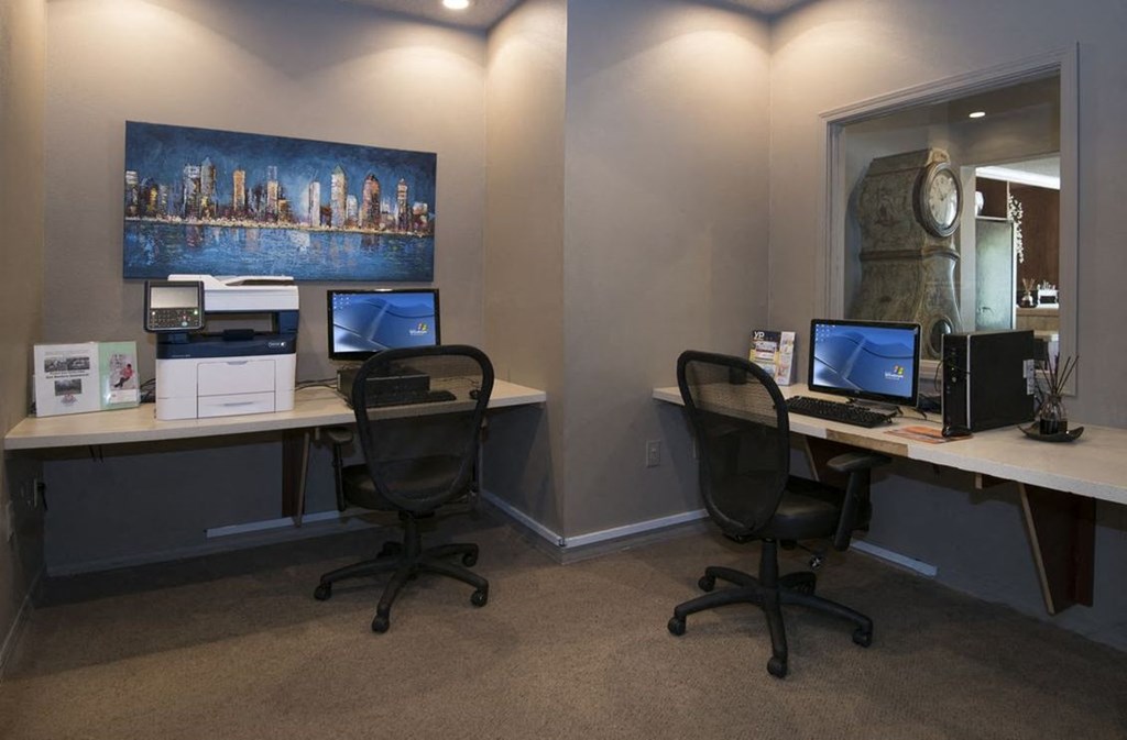 a room with two desks with computers and a painting on the wall