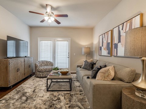 A living room with a grey couch, a wooden cabinet, a chair, a coffee table, and a ceiling fan.