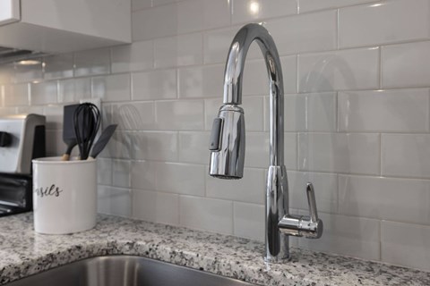 A kitchen sink with a chrome faucet and a mug with the word "bills" on it.