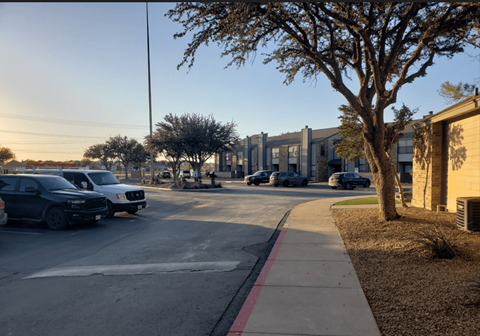 Cars parked on the side of a street with a tree and a building in the background.