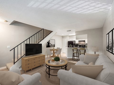 a living room with couches and a tv and a kitchen with a staircase