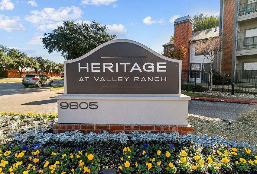 a sign for heritage at valley ranch in front of a yard with flowers