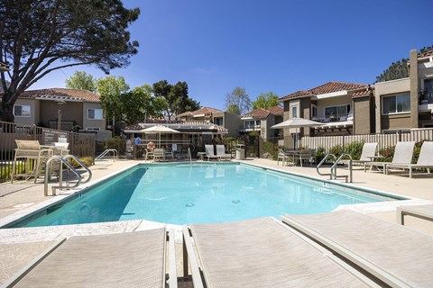 Community swimming pool with deck chairs and umbrella at Bella Del Mar Apartments, Del Mar, CA