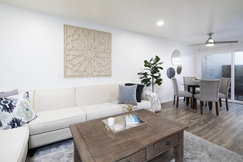 A living room with a white couch, a wooden coffee table, and a dining table with chairs.