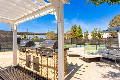 A patio with a grill and seating area under a white pergola.