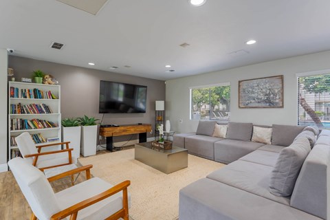 A living room with a grey couch, a white chair, a bookshelf, a television, and a painting on the wall.