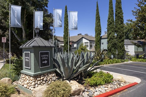 A sign for a leasing office is in front of a building with a landscaped area.