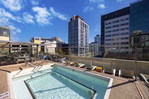 Rooftop pool deck with lounge chairs and glass railing at Urbana Apartments, San Diego, CA