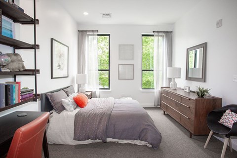 Furnished bedroom with ladder shelving and walnut dresser at Ten Front Apartments, Weymouth, Massachusetts