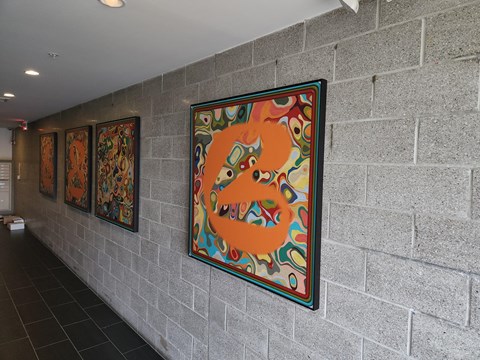 A wall with a large orange painting and three smaller paintings behind it.