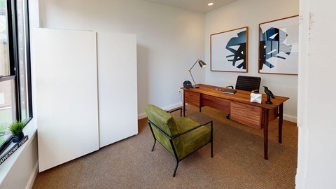 A room with a desk, chair, and two pictures on the wall.