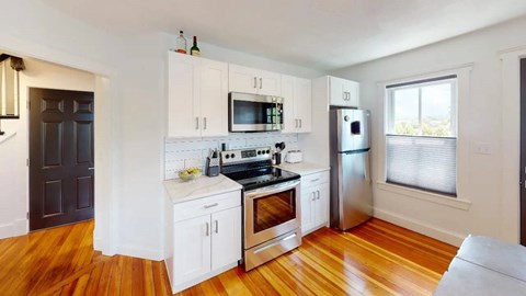 A kitchen with white cabinets and a wooden floor.