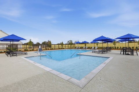 A large swimming pool surrounded by blue umbrellas and lounge chairs.