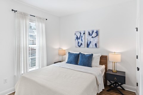 A bedroom with a bed, two lamps, and two paintings on the wall.