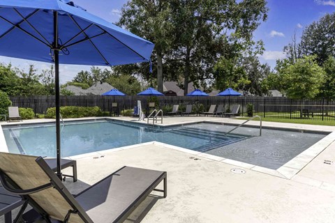 A pool with a blue umbrella and a bench.