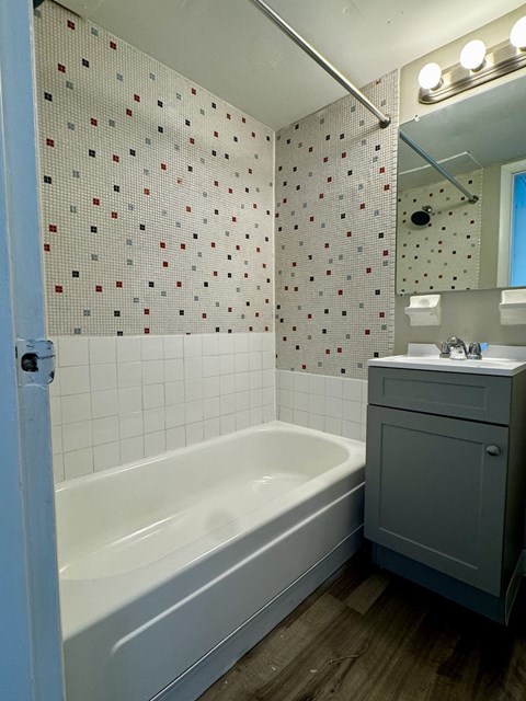 A white bathtub sits in a bathroom with a tile wall and a wooden floor.