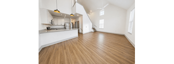 A large open space with wood-like flooring and a kitchen area with white cabinets.