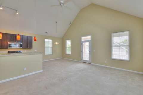 A spacious living room with a ceiling fan and a kitchen area in the background.