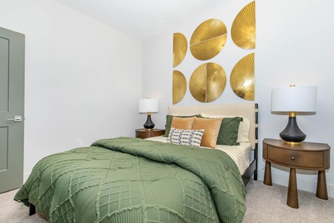 A bedroom with a bed covered in a green comforter and two lamps on bedside tables.