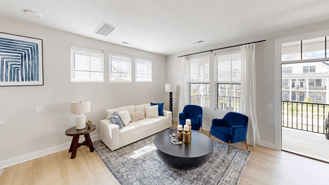 A living room with a white couch, blue chairs, and a painting on the wall.