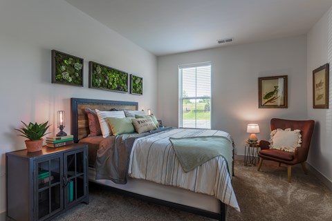 A bedroom with a bed, nightstand, and chair.