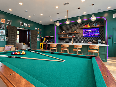 A pool table in a room with a bar and a television.