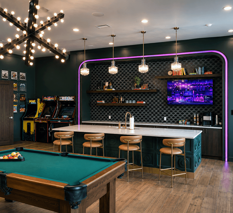 A pool table is in the middle of a room with a bar and a television.