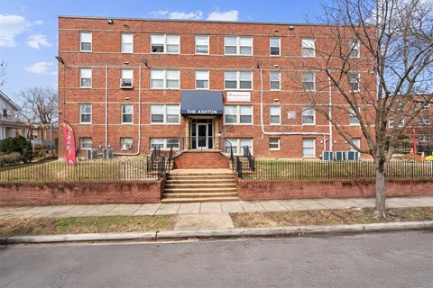 The front of a red brick building with a black gate and a tree in front.