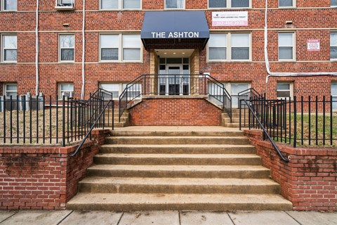 The front steps of a brick building with a sign that says The Ashton.