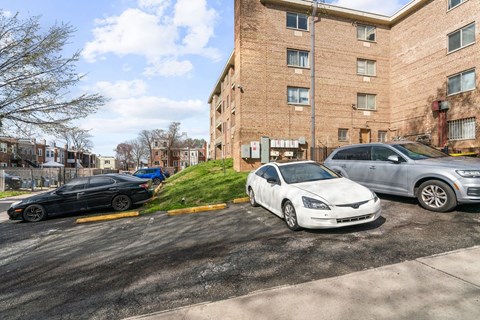 A white car is parked in a parking lot next to a brick building.