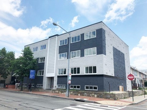 A modern building with a grey and white facade stands on a street corner.