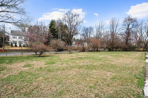 A grassy field with trees and a house in the background.