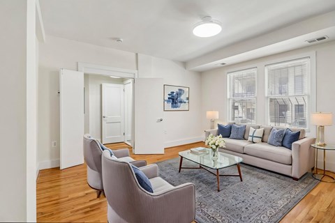 A living room with a grey couch, two grey armchairs, a glass coffee table, and a painting on the wall.