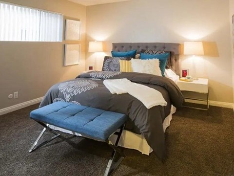 A bedroom with a bed, a bench, and two lamps.