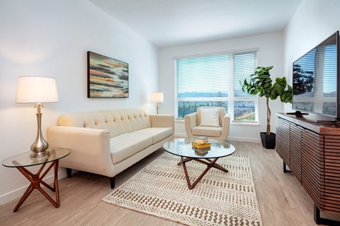 A living room with a white couch, a glass coffee table, and a painting on the wall.
