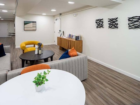 A modern living room with a grey sofa, a yellow armchair, a round table with a plant on it, and a wooden sideboard with magazines.