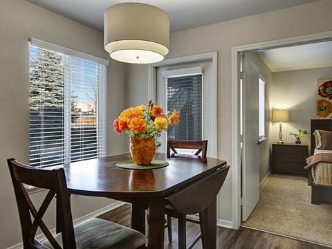 A dining room with a table and chairs and a vase of flowers on the table.