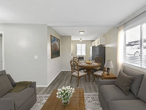 A living room with a grey couch, a wooden table with a vase of flowers, and a painting on the wall.
